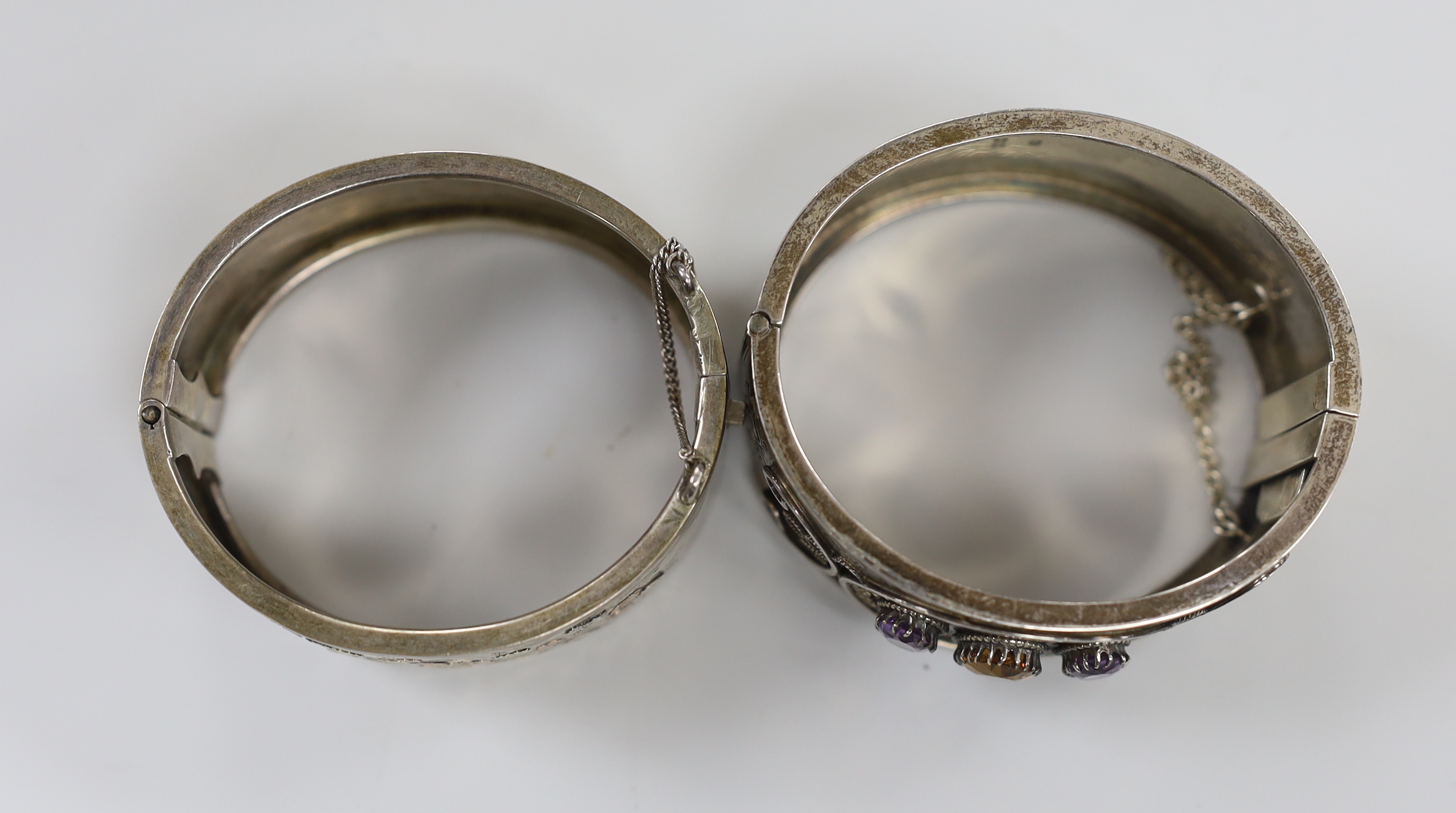 A late Victorian silver and three stone amethyst and citrine set hinged bangle and a later white metal bangle.